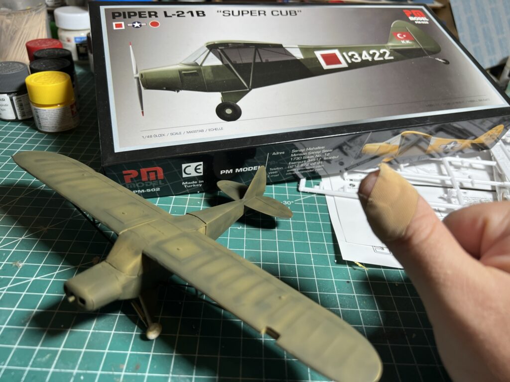 Kesim matı üzerinde, kit kutusunun yanında kısmen boyanmış PM Model Piper L-21B maketi.