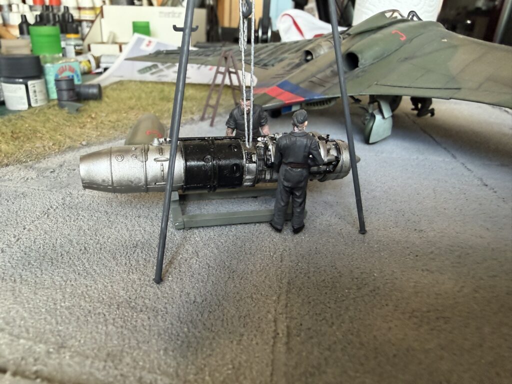 Two ground crew figures working on the Jumo 004 under the hoist